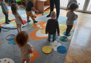 Dzieci skaczą po kolorowych kółkach i rzucają piłką do celu